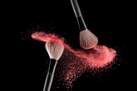 36085973 - make-up brush with pink powder explosion on black background